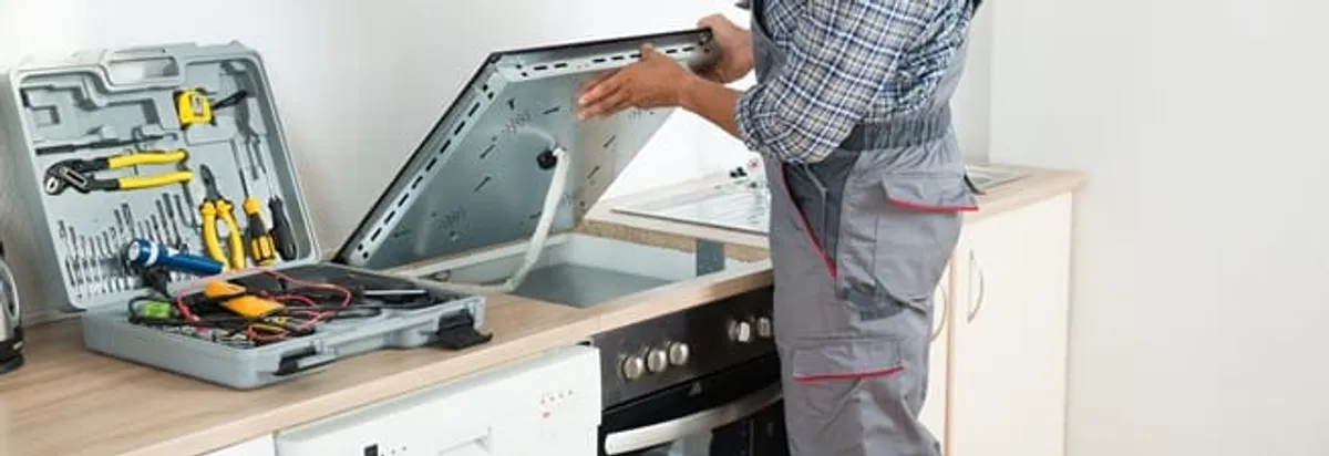Cooktop repair technician lifting a built-in stovetop for service in Myrtle Beach, SC