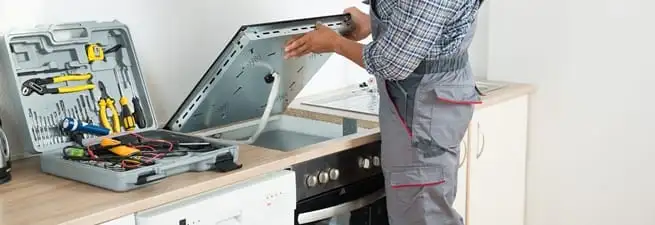 Cooktop repair technician lifting a built-in stovetop for service in Myrtle Beach, SC