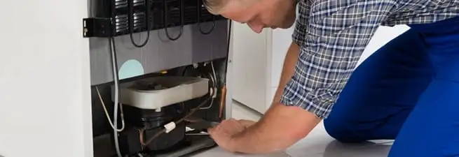 Refrigerator repair technician servicing the compressor and condenser area in Myrtle Beach, SC