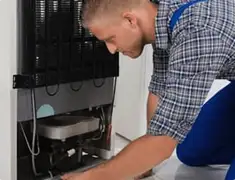 Refrigerator repair technician servicing the compressor and condenser area in Myrtle Beach, SC